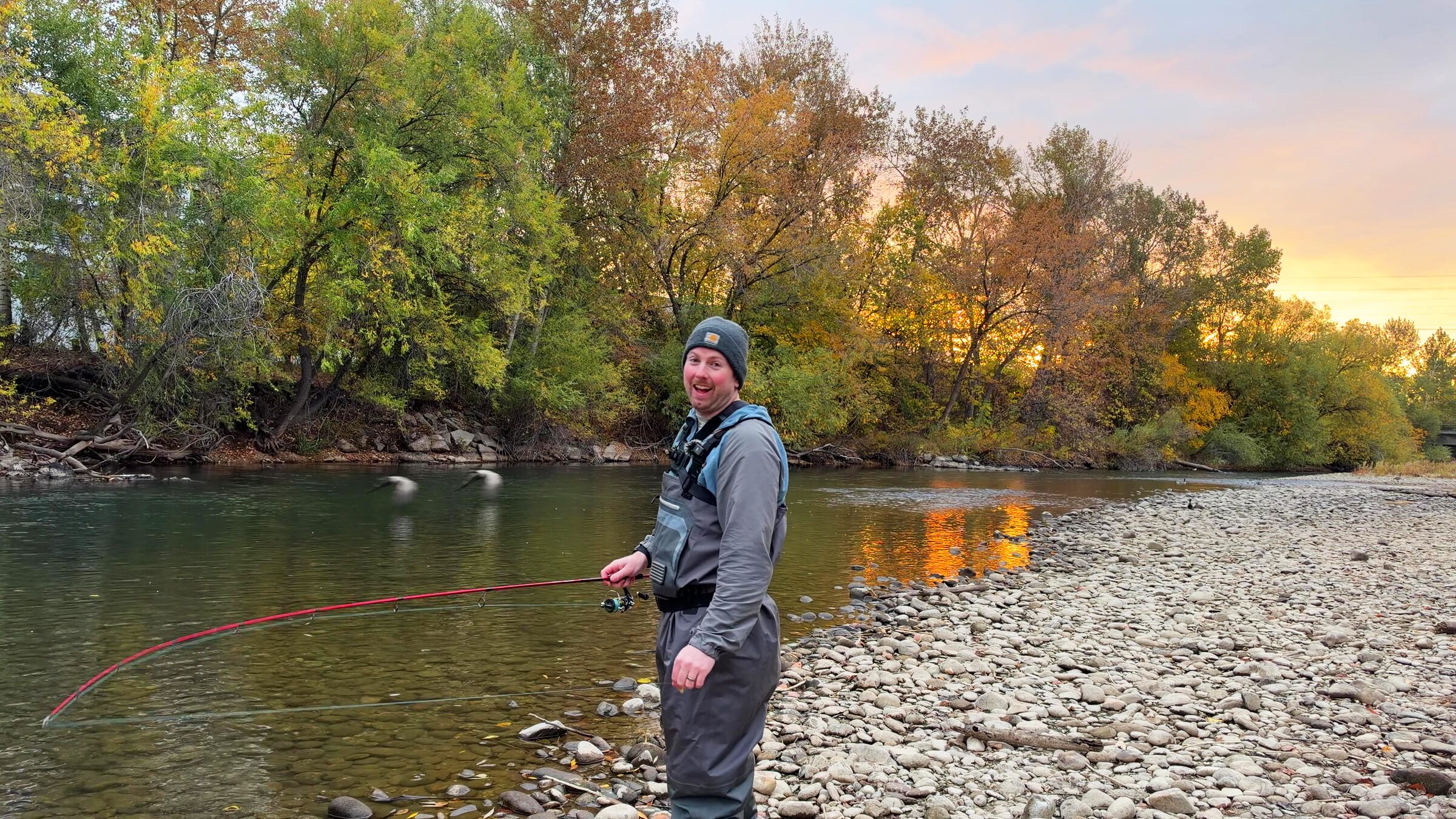 Zack in waders on the Boise River at sunrise, smiling back at the camera